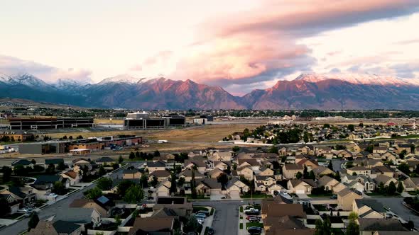 Aerial hyperlapse of a suburban community in a valley with snow-capped mountains in background at su