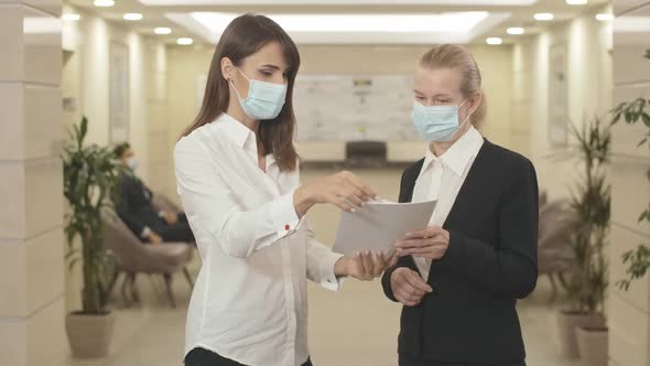 Young and Mid-adult Women in Face Masks Discussing Project in Office. Portrait of Serious Business