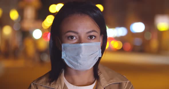 Bokeh Shot of Young Afro Woman in Safety Mask Looking at Camera Standing Outdoors