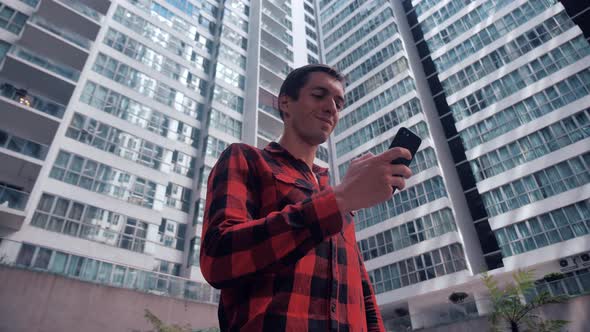 Young Man in Plaid Shirt Using App on Smart Phone in City