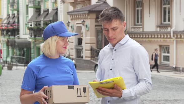 Handsome Young Man Signing Papers Receiving a Package From Delivery Woman