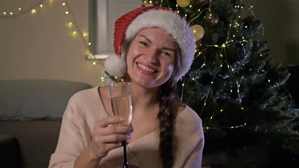 Beautiful Cheerful Woman in Santa Hat with a Glass of Champagne. Against the Background of a