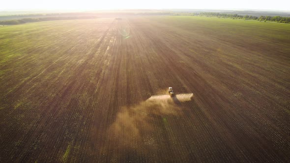 Aerial View of Farming Tractor Spraying on Field with Sprayer, Herbicides and Pesticides at Sunset