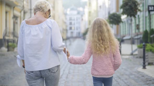 Camera Follows Carefree Caucasian Grandmother and Granddaughter Strolling on Sunny City Street and