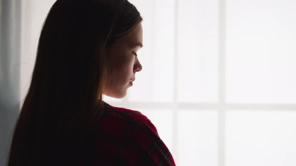 Elegant Young Woman Stands Near Window in Room Backside View