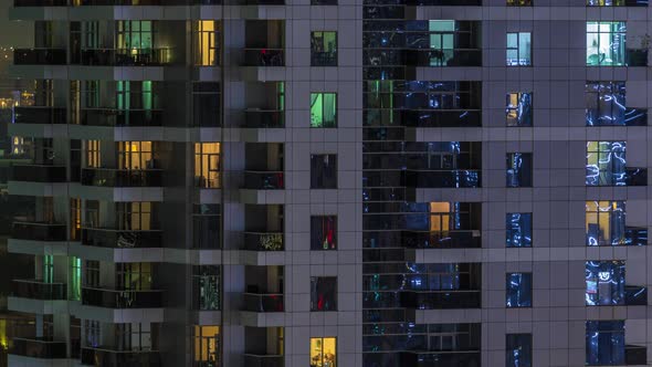 Rows of Glowing Windows with People in Apartment Building at Night