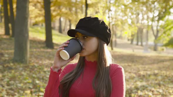 Attractive Girl Stands in Pose and Drinks a Cup of Tea in Sunny Autumn Park