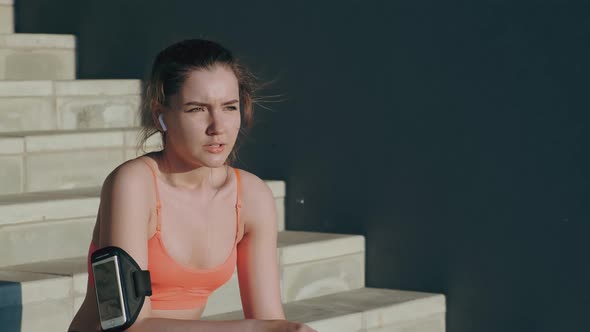 Girl with Phone on Arm Sits on Steps After Running Slow Motion