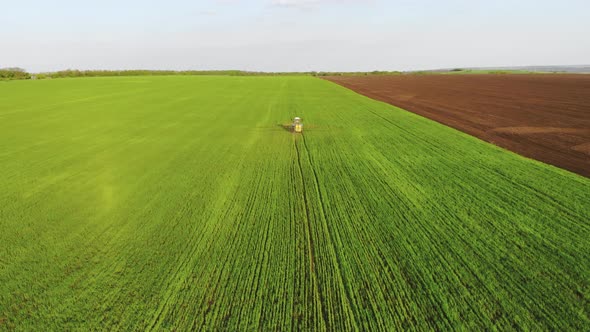 Aerial View of Farming Tractor Spraying on Field with Sprayer, Herbicides and Pesticides at Sunset