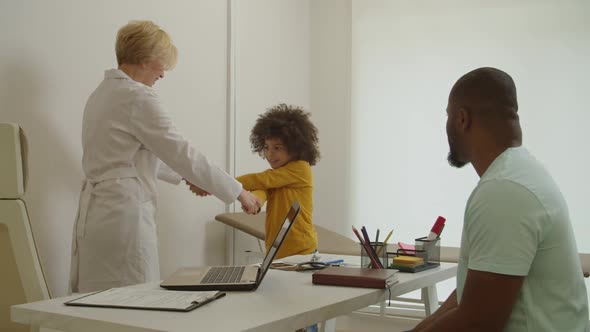 Carefree Woman Doctor and Cute Little African American Boy Giving High Five in Medical Office