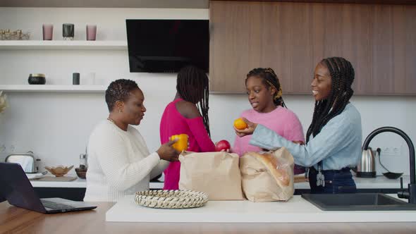 Cheerful Black Teenage Sisters Unpacking Grocery Bags with Mom