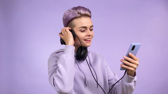 Young Woman in All Purple Listening Music Via Smartphone Headphones