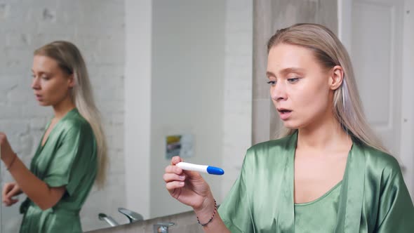 Shocked Woman Holding Positive Pregnancy Test in Bathroom