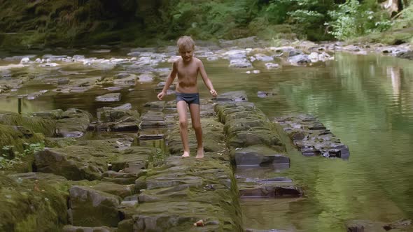 Boy Walks on Rocks in Water in Wild Forest