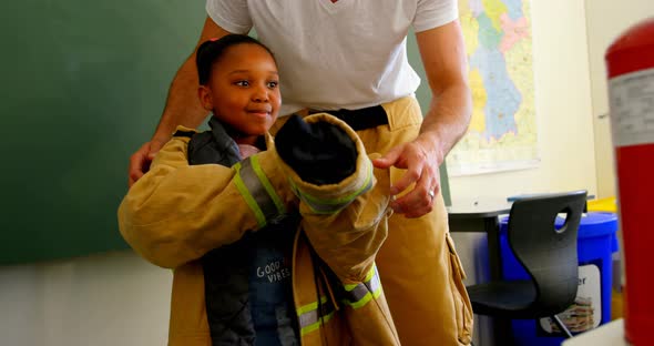 Male firefighter  helping African American girl to wear fire uniform in classroom. Schoolgirl smilin