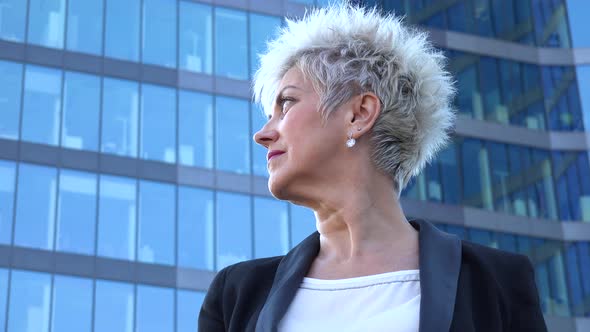 A Middle-aged Businesswoman Looks Around in an Urban Area - a Windowed Office Building