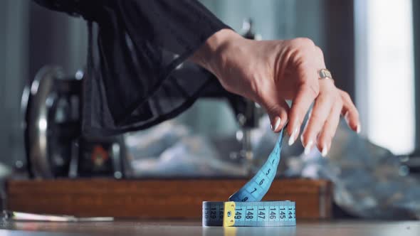 Seamstress is taking up blue tape measure on the background of sewing machine