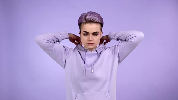 Young Woman Putting on Hood of Sweatshirt Folding Arms Crossed Indoors