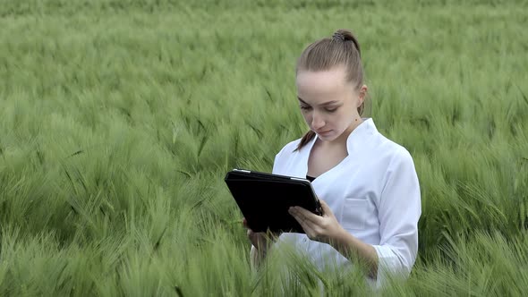 Farmer wearing white bathrobe is checking harvest progress on a tablet at the green wheat field