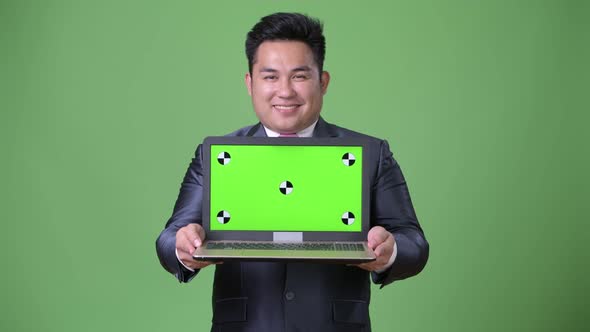 Young Handsome Overweight Asian Businessman Against Green Background