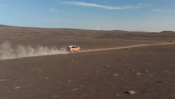 Birds Eye Drone Following Car Speeding Along Dirt Road in Iceland Rocky Desert Stirring Up Dust