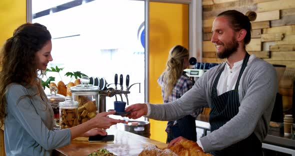 Waiter serving coffee to female costumer at counter