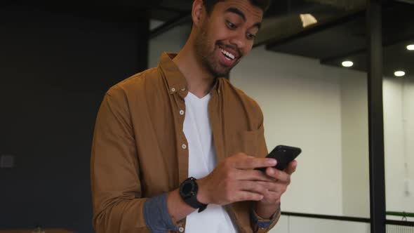 Mixed race businessman standing using a smartphone in a modern office