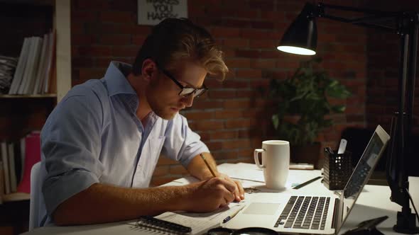 Young Architect with Blue Shirt and Light Beard Drawing with Pencil and Triangle Wearily Taking Off