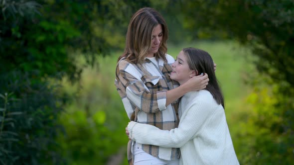 Loving tender mum hugging with a cute daughter on a field at sunset