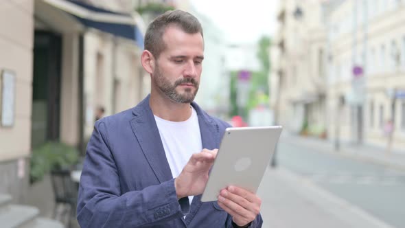 Mature Adult Man Browsing Internet on Tablet Outdoor