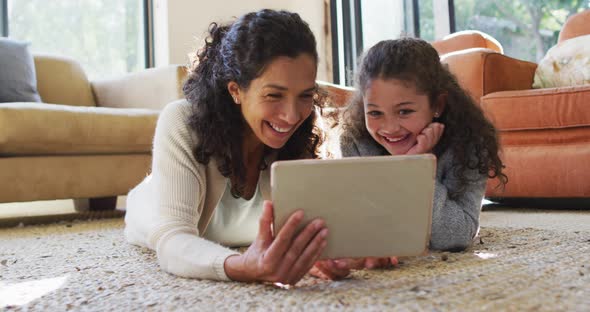 Happy mixed race mother and daughter laying on the floor,having fun and using tablet