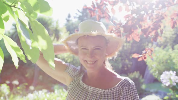 Portrait of happy caucasian senior woman walking in garden wearing sunhat and smiling in the sun