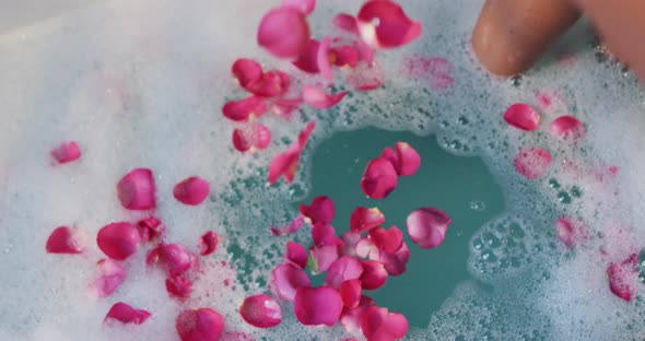 African american woman taking bath and touching flower petals in water in bathroom