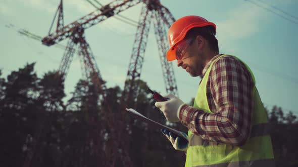 Electrical Engineer Wearing Hard Hat and Safety Vest Checking Electrical Systems on High Voltage