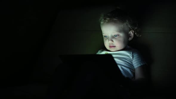 Little girl watching cartoons on a tablet in the dark