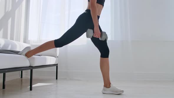 Brunette in Black Sportswear in a White Apartment Makes a Split Squat with Dumbbells in Her Hands