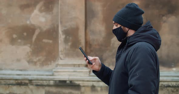 Side View of Man Walking and Using His Smartphone for Communicating in Social Networks. Guy in Black