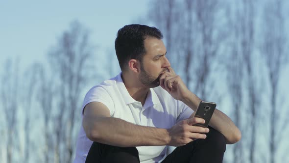 Thoughtful Bearded Guy with Smartphone Sitting on Stairs in Park