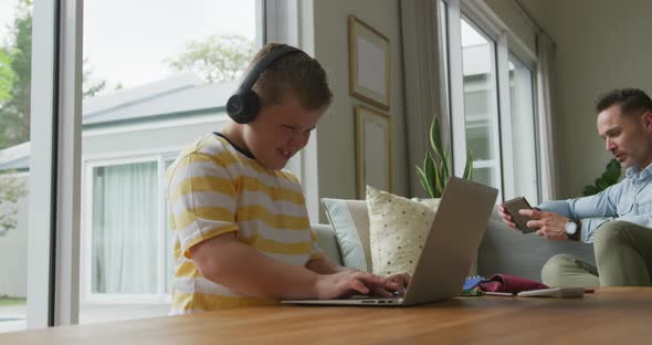 Caucasian father with son sitting in living room, using laptop and smartphone