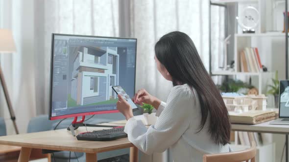 Asian Woman Engineer Using Smartphone While Designing House On A Desktop At Home