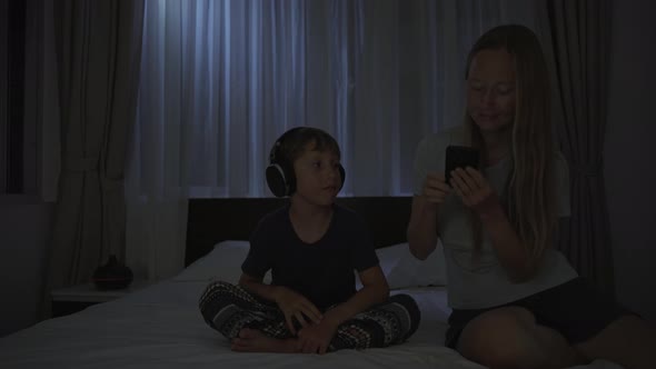 A Woman at Night Turns on a Meditation Relaxation Application on Her Phone for Her Son to Relax