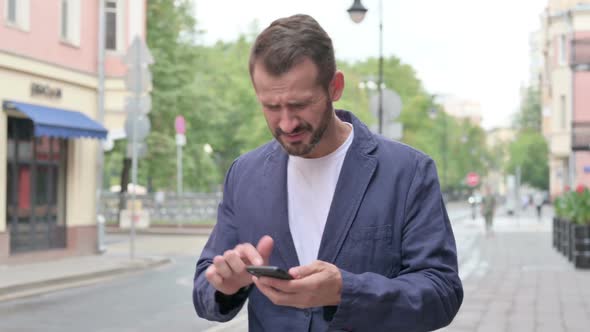 Man Reacting to Loss on Phone While Walking Down the Street