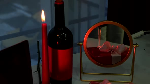 Online Date Concept Red Candles Bottle of Wine and Present Gift in Front of Laptop