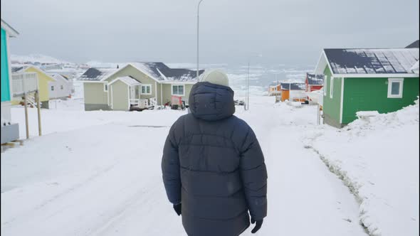 Man In Winter Coat Walking Through Snow Covered Street Of Ilulissat