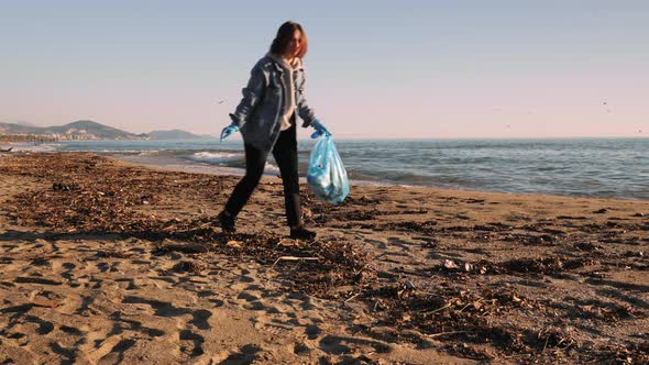 Girl volunteer picking up plastic bottles trash left on beach, keeping beach clean.