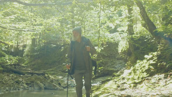 Old Man Tourist with a Backpack Walks in the Valley By the River on a Sunny Day