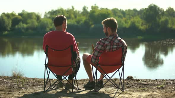 Childhood Friends Sitting on River Bank, Drinking Beer and Discussing Fishing