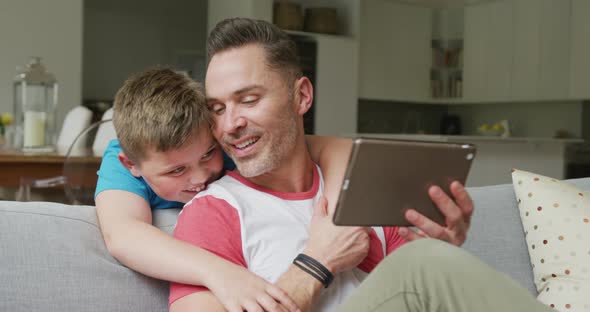 Happy caucasian father with son sitting in living room and using tablet