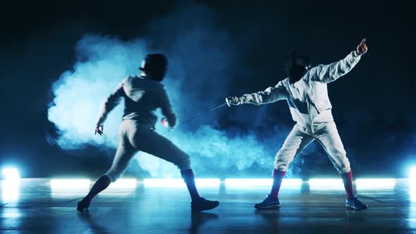 Fencing Practice of Two Sportsmen in a Dark Hall