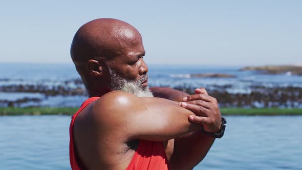 Senior african american man exercising stretching on rocks by the sea